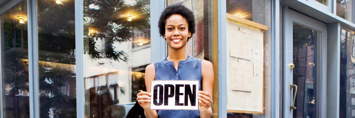 A woman stnading outside her storefront holding a sign that says "open"